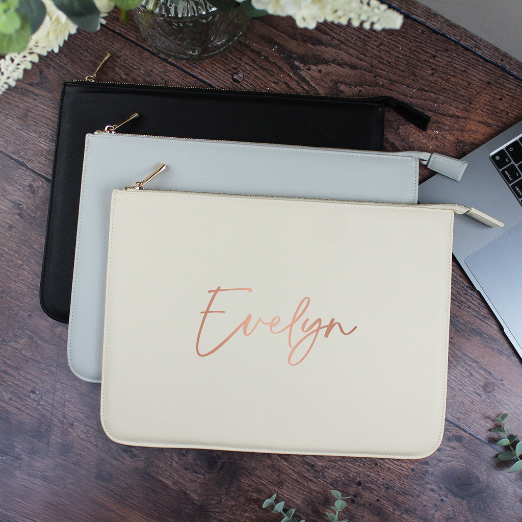 Beige pouch with 'Evelyn' embroidery on a wooden surface with laptop and other pouches.