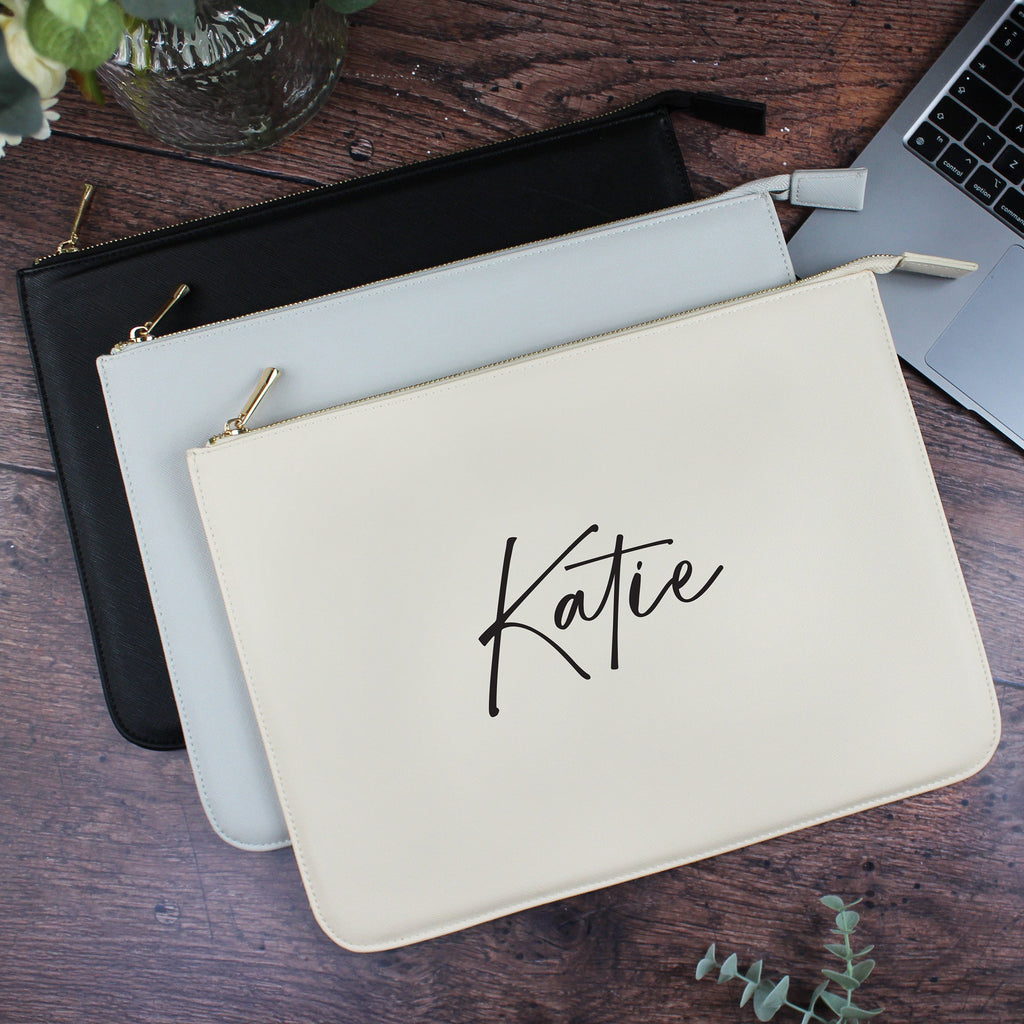 Beige pouch with 'Katie' branding on a wooden surface with a laptop and flowers.