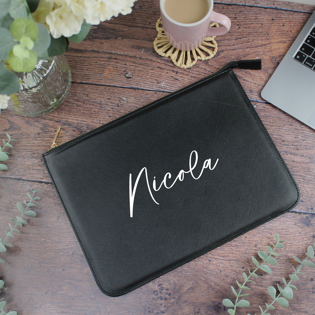 Black pouch with 'Nicola' printed on it on a wooden surface with a cup and laptop.