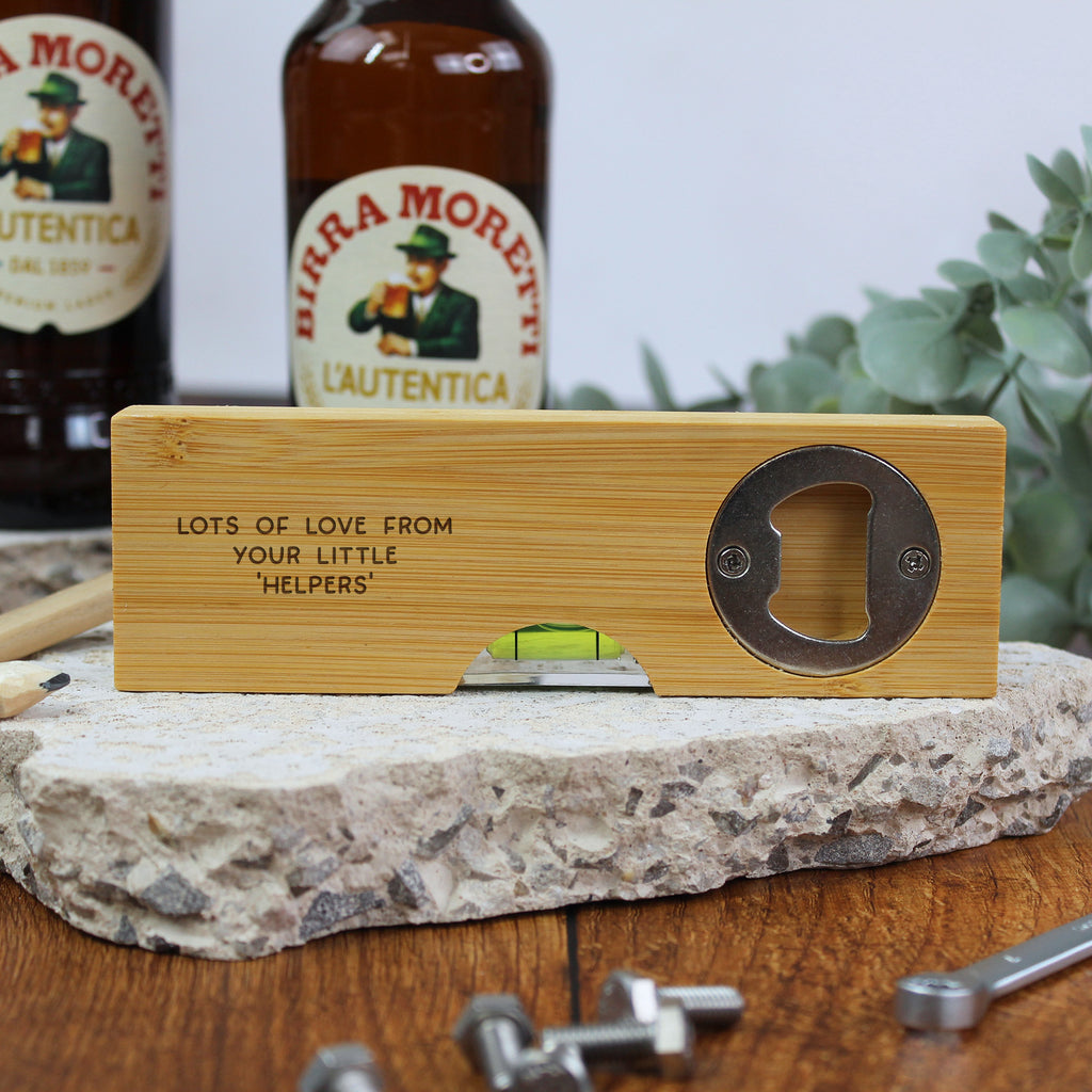 Wooden bottle opener with engraved text on a stone surface with bottles in the background