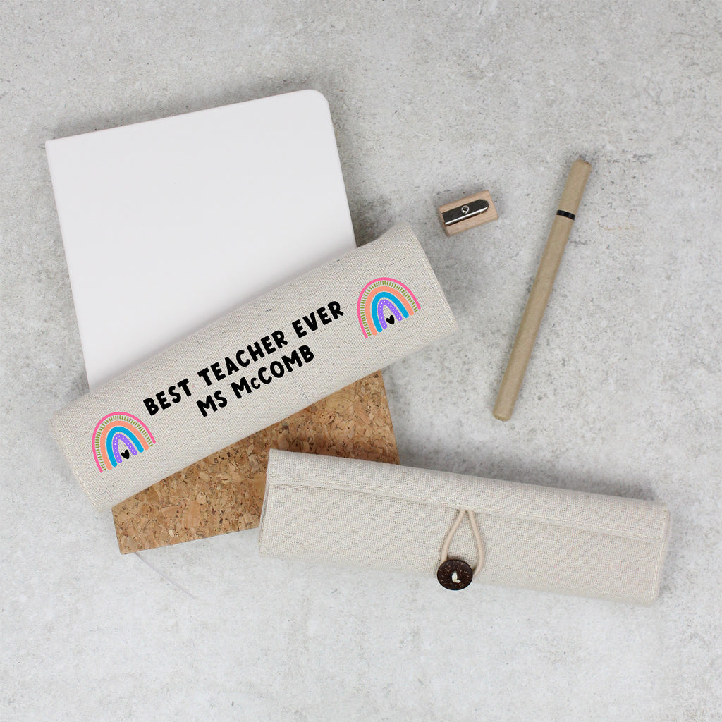 Personalized pencil case with rainbow design and text on a gray surface with paper and pen.