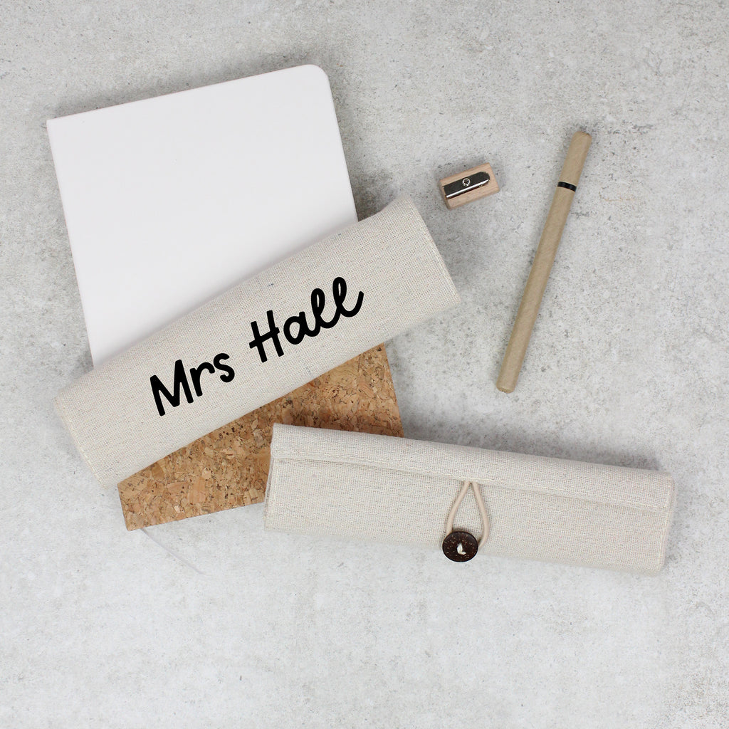 Personalized pencil case with 'Mrs Hall' on a gray surface with stationery items.