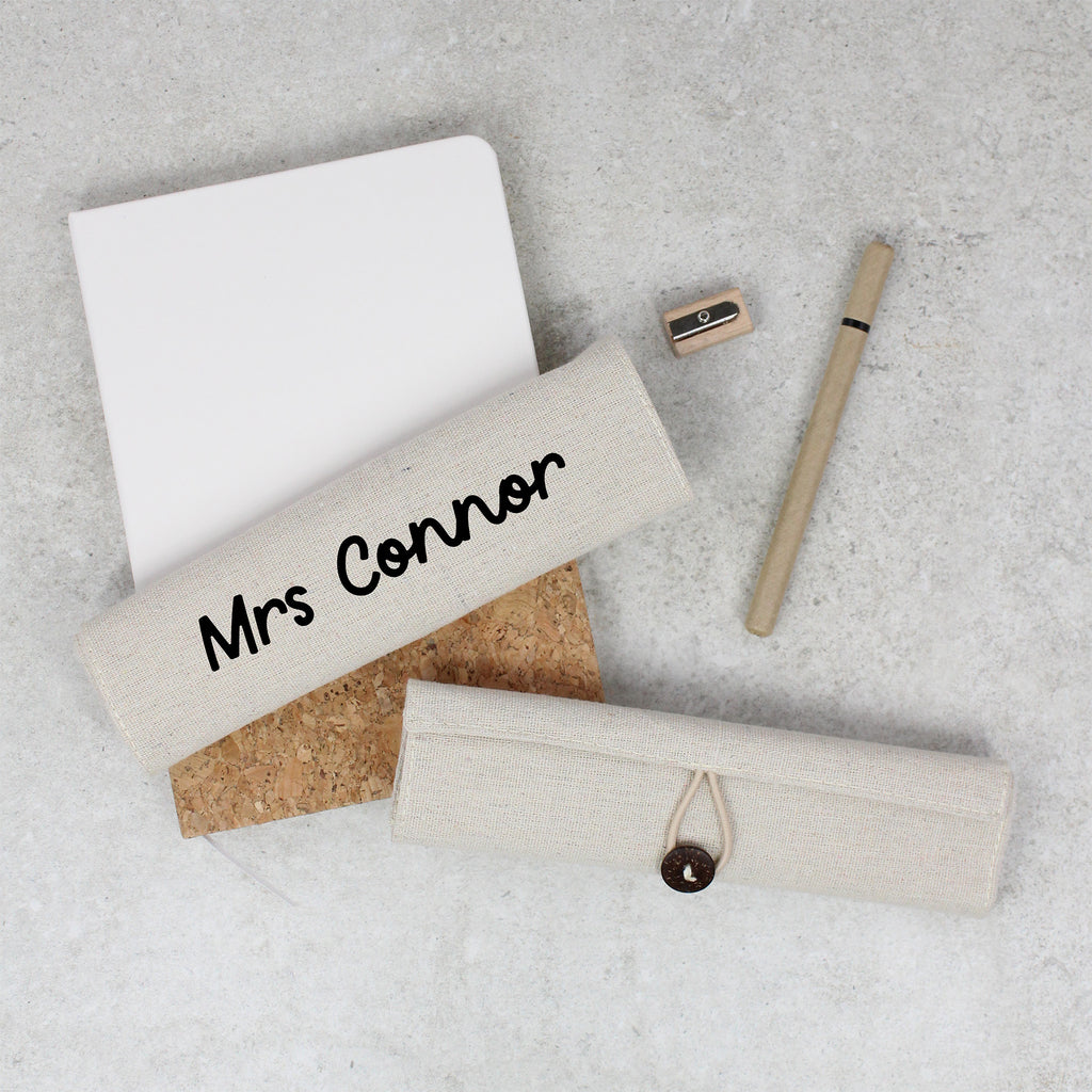 Personalized name tag with 'Mrs Connor' on a cork board, with a pen and sharpener on a light gray surface.