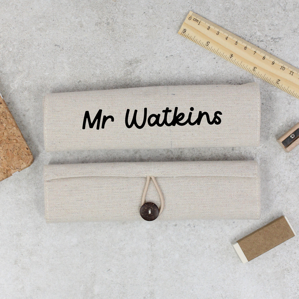 Beige clutch bag with 'Mr Watkins' text on a gray surface with a ruler and cork board.