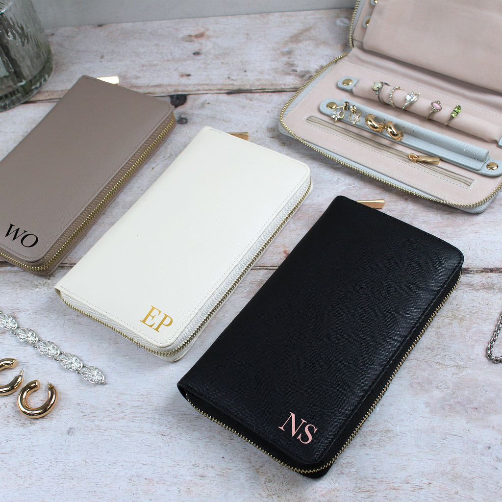 Three wallets with initials on a wooden surface, surrounded by jewelry.