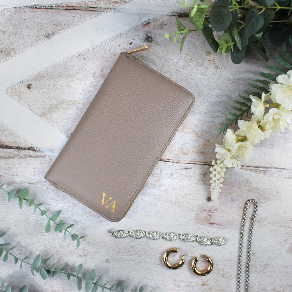 Brown wallet with 'VA' initials, jewelry, and flowers on a wooden surface