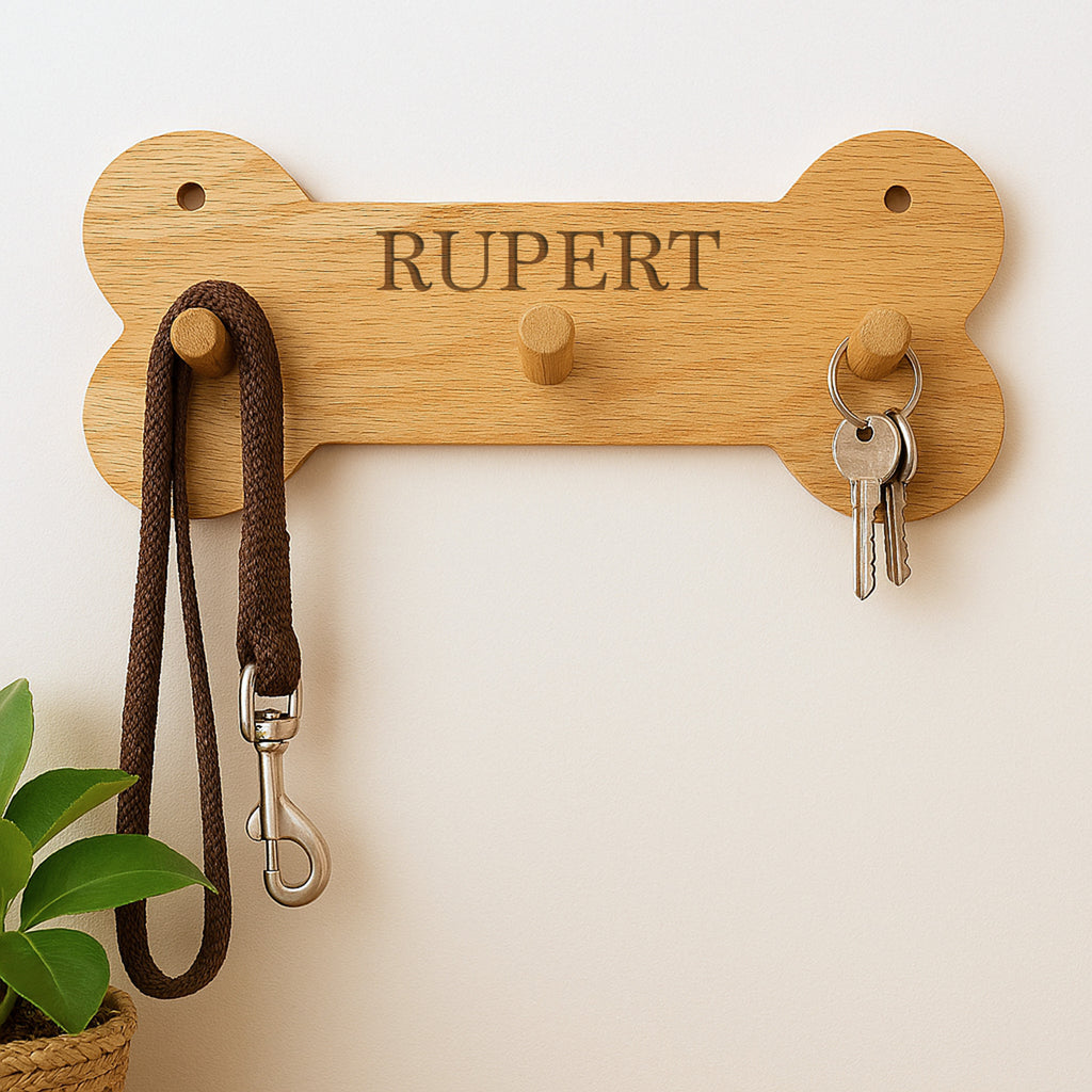 Wooden bone-shaped key holder with 'RUPERT' engraving, holding a dog leash and keys on a light background.