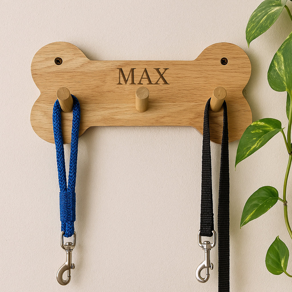 Wooden bone-shaped leash holder with 'MAX' engraving, holding two dog leashes against a beige wall.