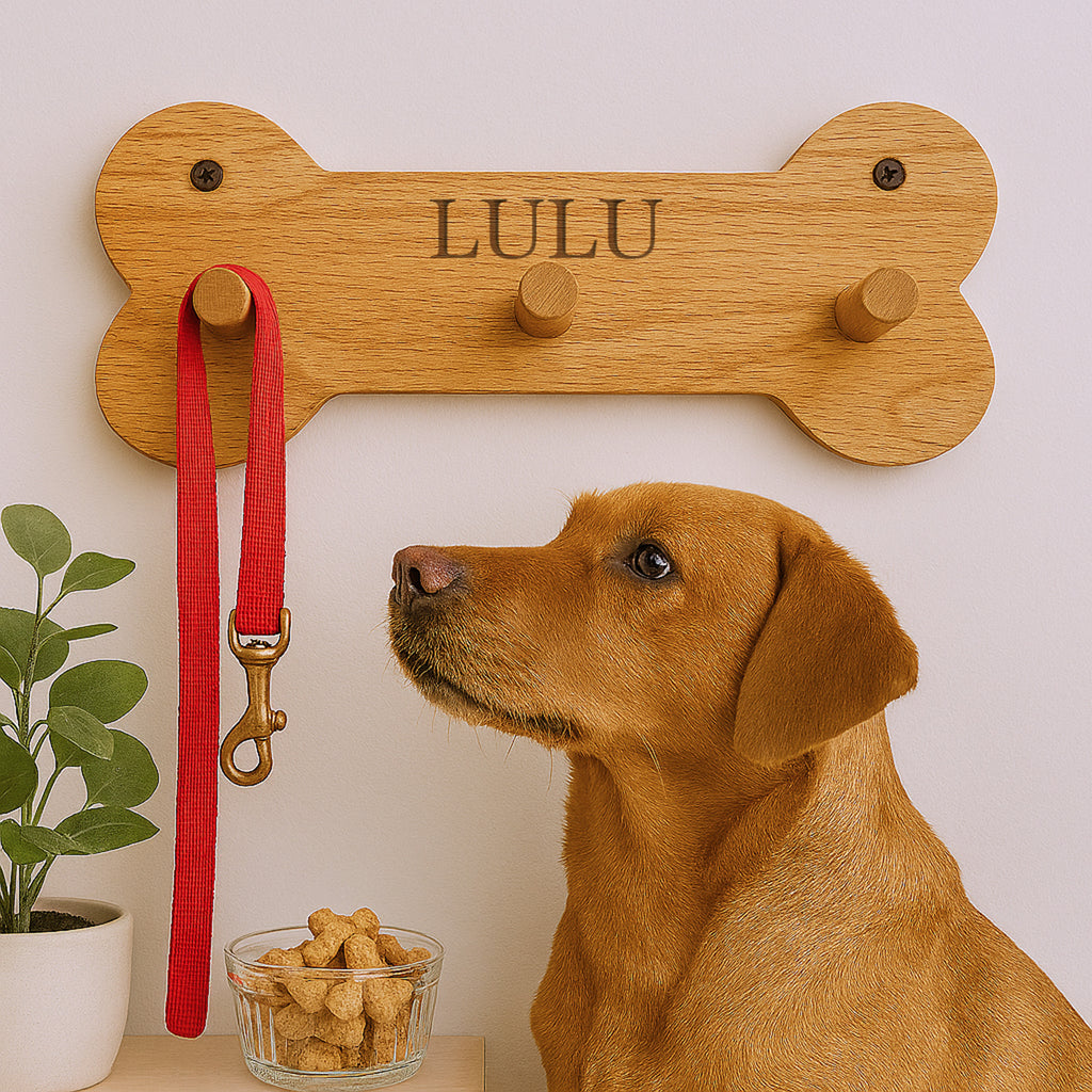 Dog looking at a wooden bone-shaped leash holder with 'LULU' engraved, next to a red leash and a bowl of dog treats.