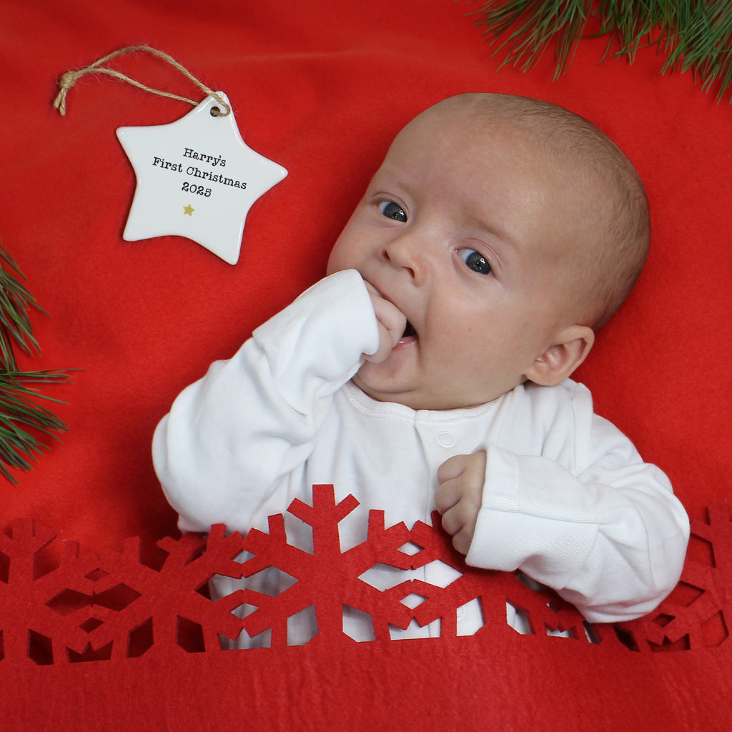 Baby lying on a red surface with a Christmas-themed decoration, including a star-shaped tag and snowflake cutout.