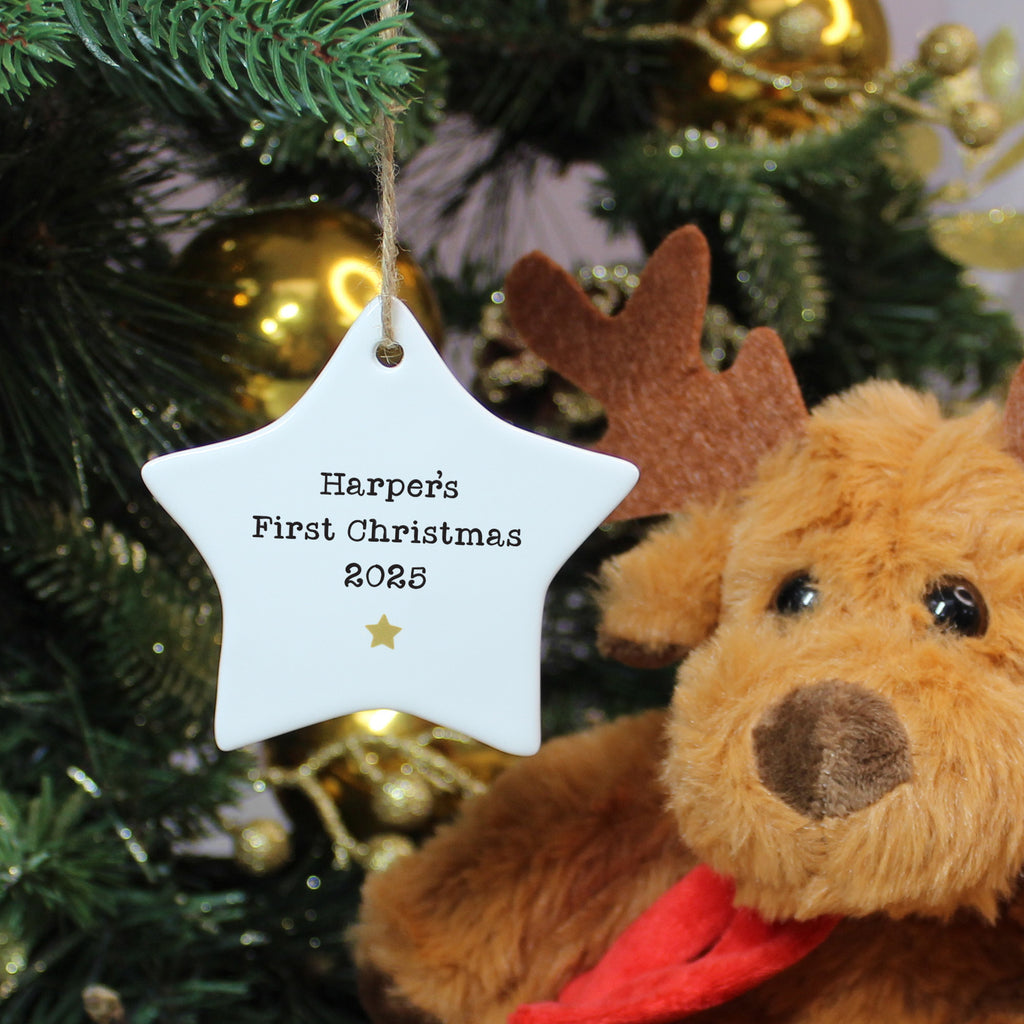 Star-shaped ornament with 'Harper's First Christmas 2025' text, teddy bear in front of a decorated Christmas tree.