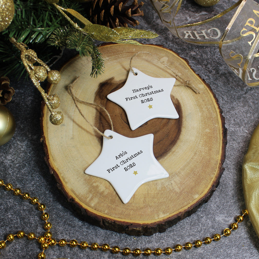 Two star-shaped 'First Christmas' tags on a wooden disc with festive decorations.