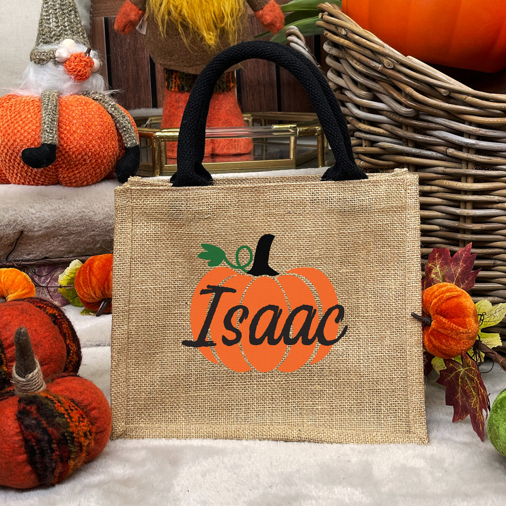 Jute bag with pumpkin design and 'Isaac' text, surrounded by autumn decorations.