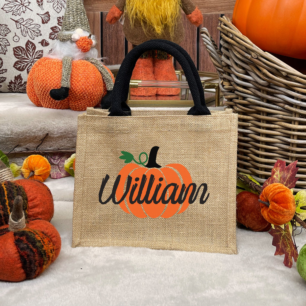 Jute bag with pumpkin design and 'William' text, surrounded by autumn decorations.