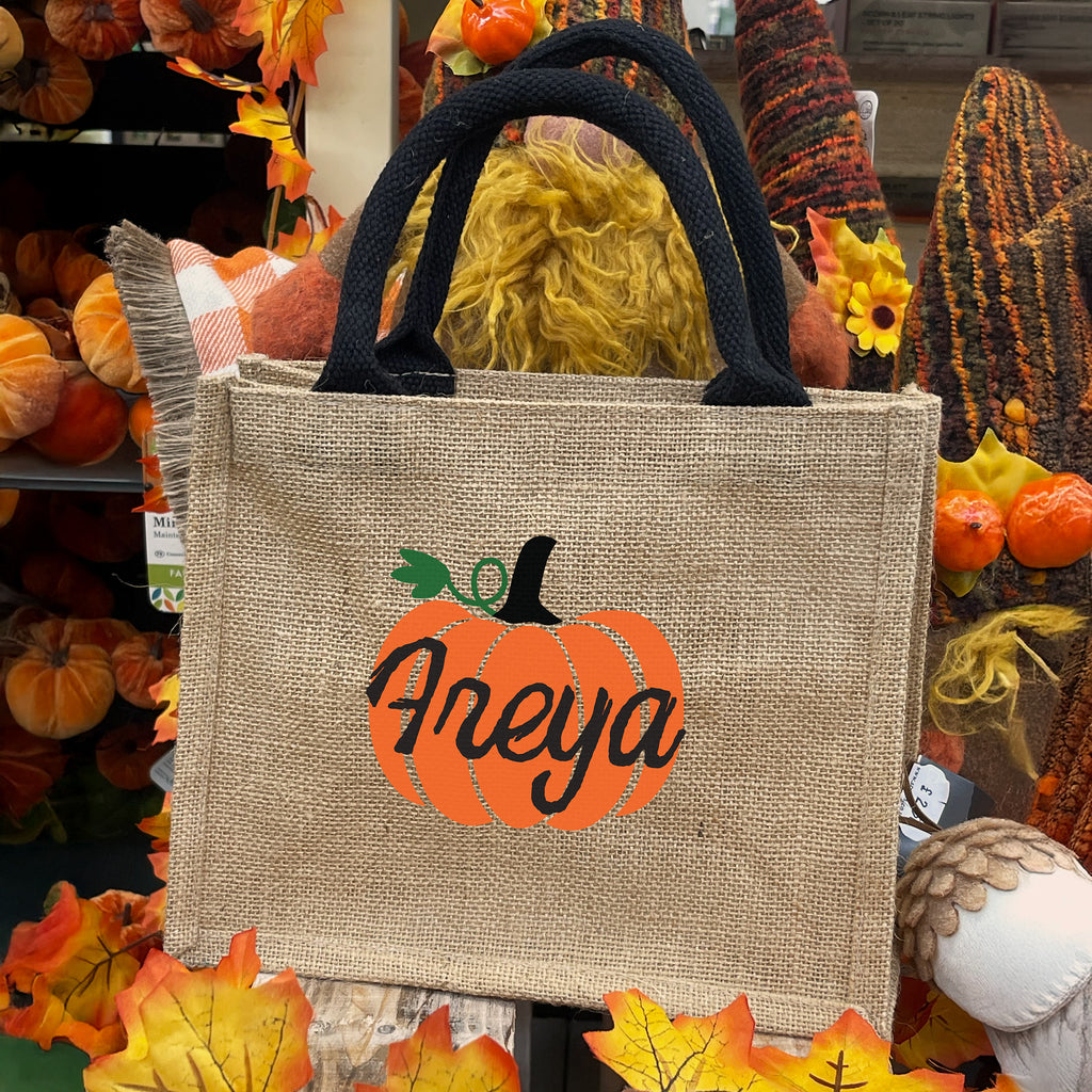 Burlap tote bag with pumpkin design and 'Aleya' text, surrounded by autumn decorations.