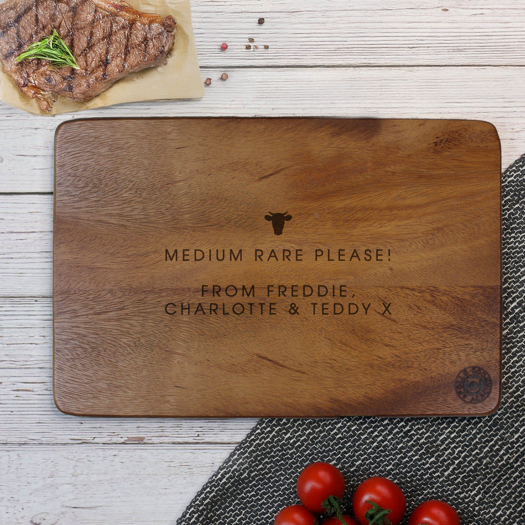 Wooden cutting board with engraved text on a wooden surface with a steak and tomatoes.
