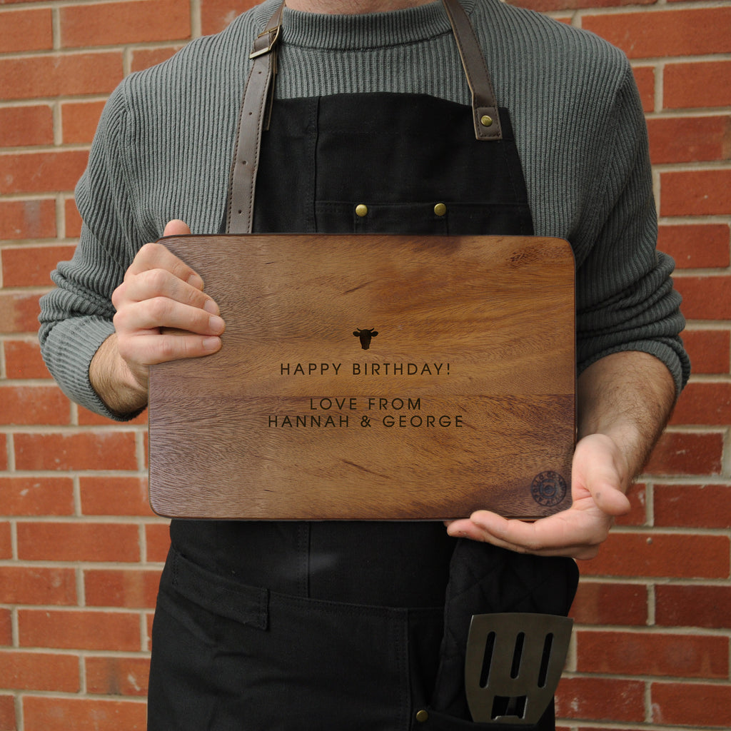 Person holding a wooden cutting board with engraved text against a brick wall.