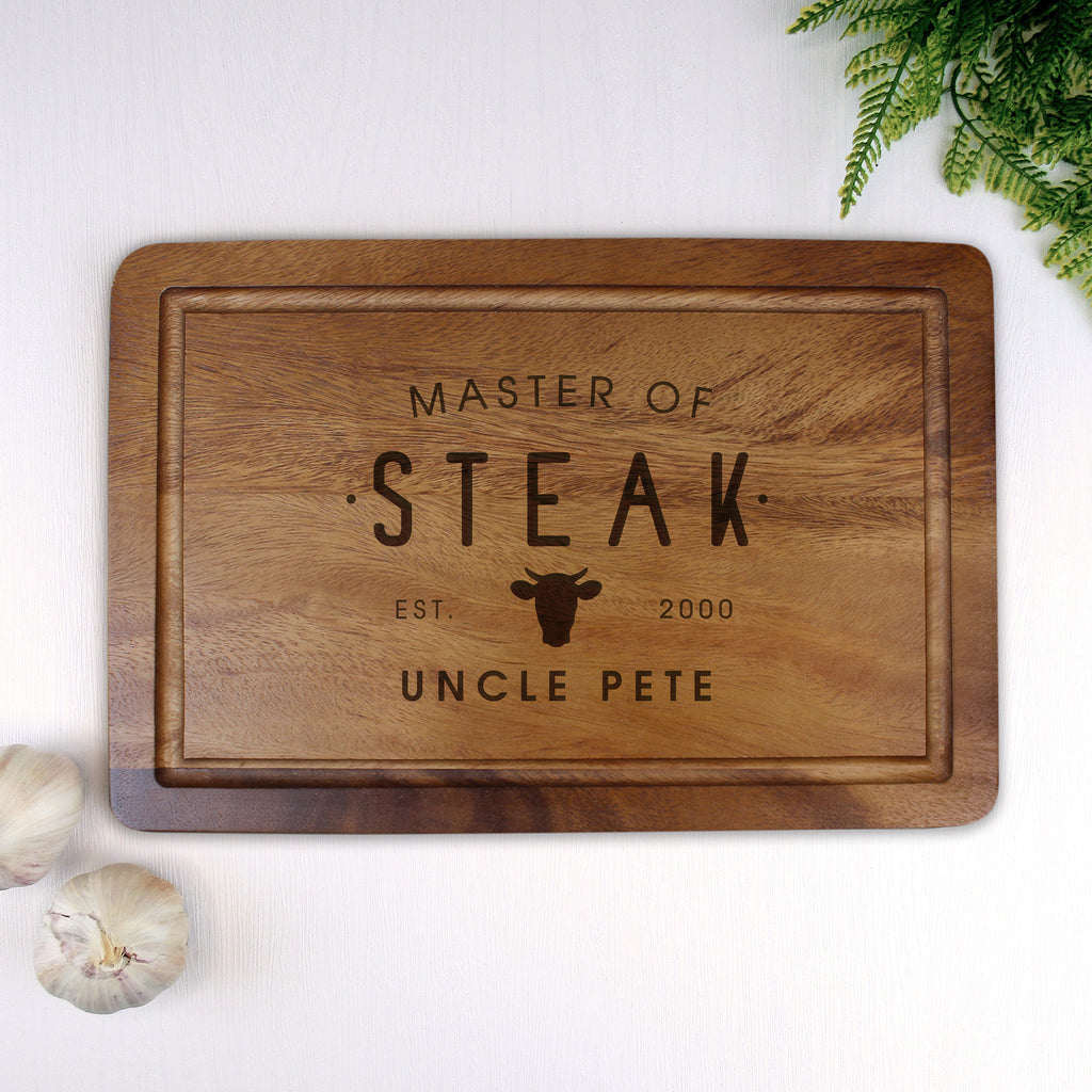 Wooden cutting board with engraved text on a white surface with garlic and a plant.