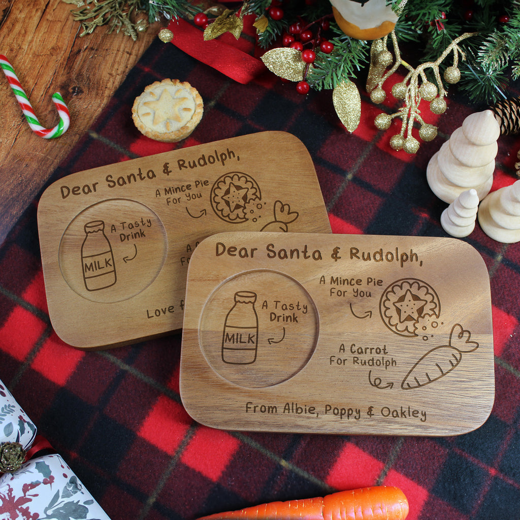 Two wooden coasters with Santa and Rudolph text on a festive background with Christmas decorations.
