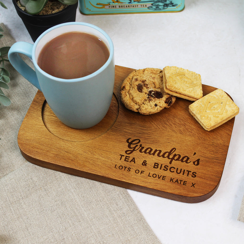 Mug of tea with cookies on a wooden board engraved with 'Grandpa's Tea & Biscuits' on a light background.