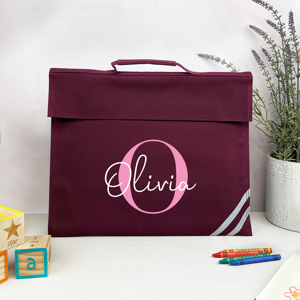 Maroon bag with 'Olivia' monogram on a white surface with toys and a plant.