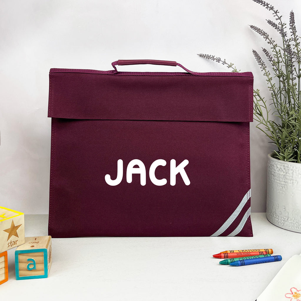 Maroon bag with 'JACK' printed on it, placed on a white surface with toys and a plant in the background.