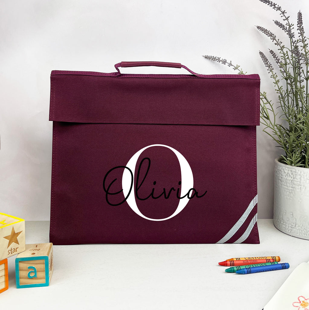 Maroon bag with 'Olivia' printed on it, placed on a white surface with crayons and a plant in the background.