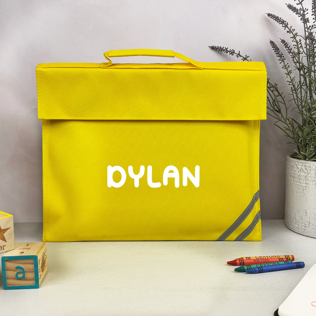 Yellow bag with 'DYLAN' printed on it, placed on a surface with crayons and blocks around.