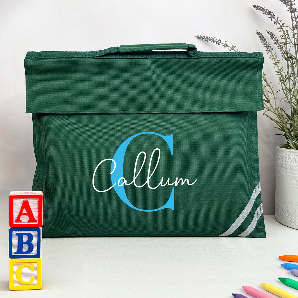 Green bag with 'Callum' printed on it, surrounded by colorful blocks and crayons on a white surface.