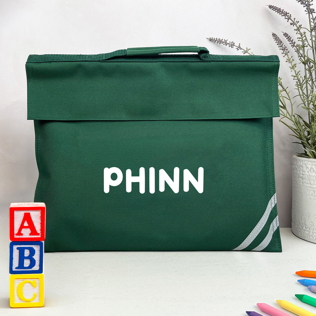 Green bag with 'PHINN' branding on a white surface with colorful blocks and crayons.