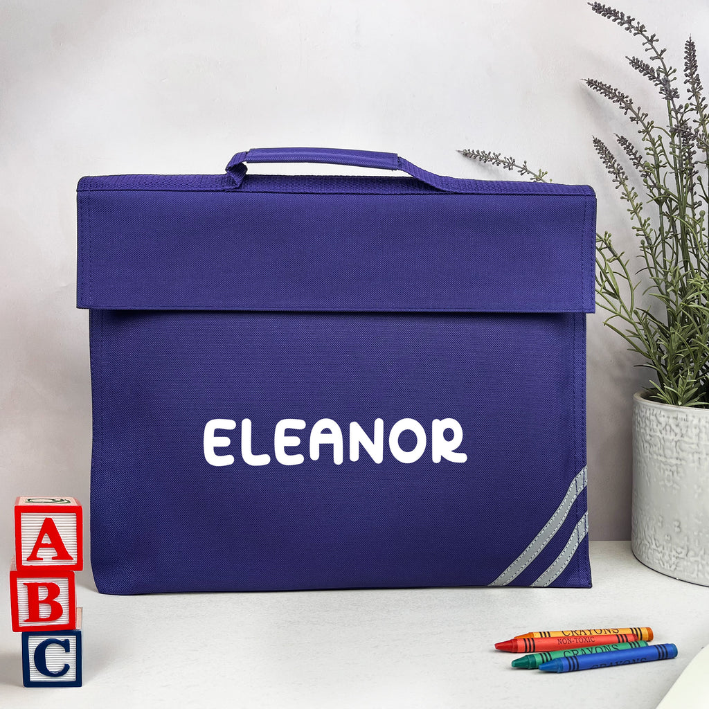 Blue bag with 'Eleanor' printed on it, placed on a white surface with colorful crayons and letter blocks.