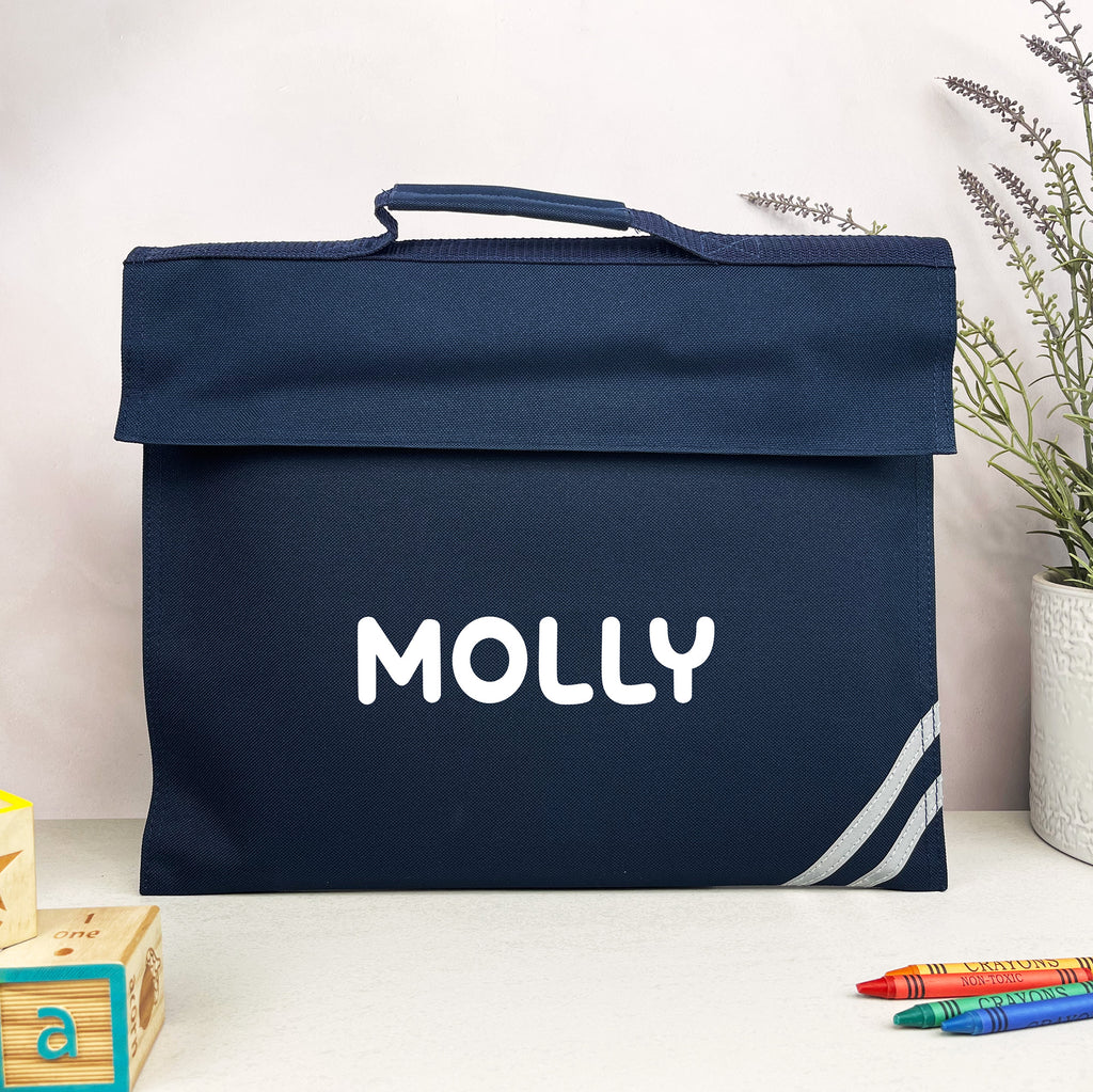 Navy blue bag with 'MOLLY' printed on it, placed on a white surface with a plant and crayons in the background.