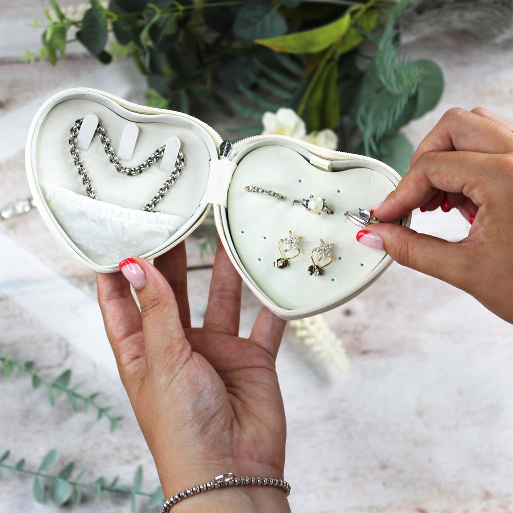 Heart-shaped jewelry box with earrings and a necklace, held by two hands against a blurred natural background.