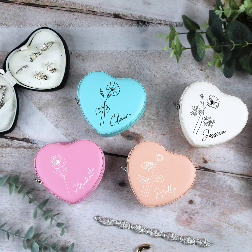 Heart-shaped jewelry cases with names engraved on a wooden surface with greenery.