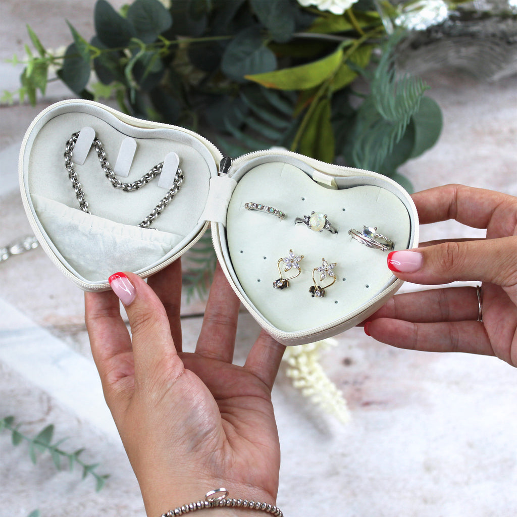 Heart-shaped jewelry box with earrings held by a hand against a natural background