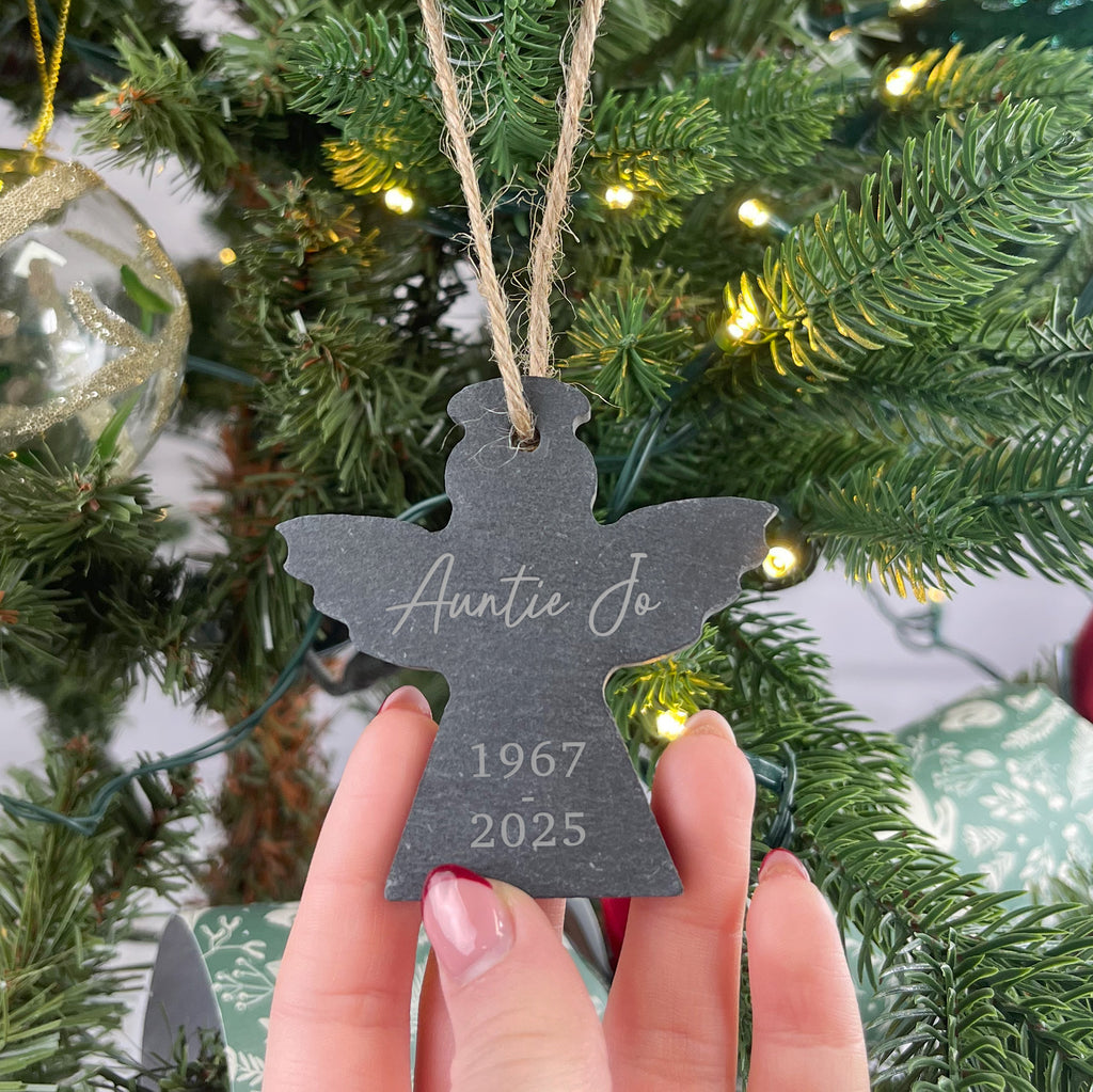 Decorative ornament with 'Auntie Jo' and year details held in front of a Christmas tree.