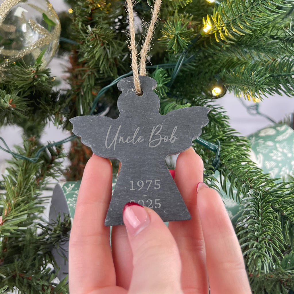 Hand holding a personalized Christmas ornament with 'Uncle Bob' and year details against a Christmas tree background.