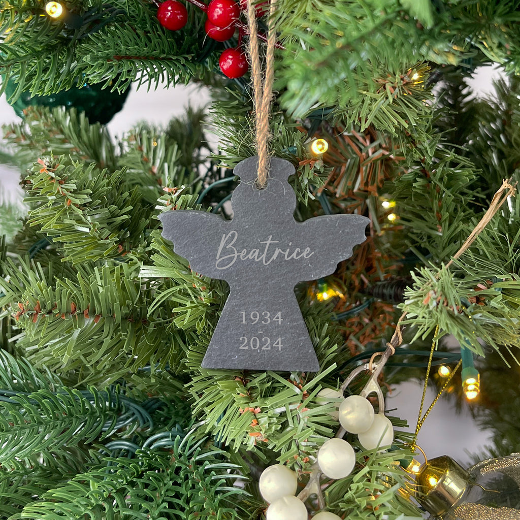 Christmas tree ornament with 'Beatrice' and years engraved, hanging among green branches.