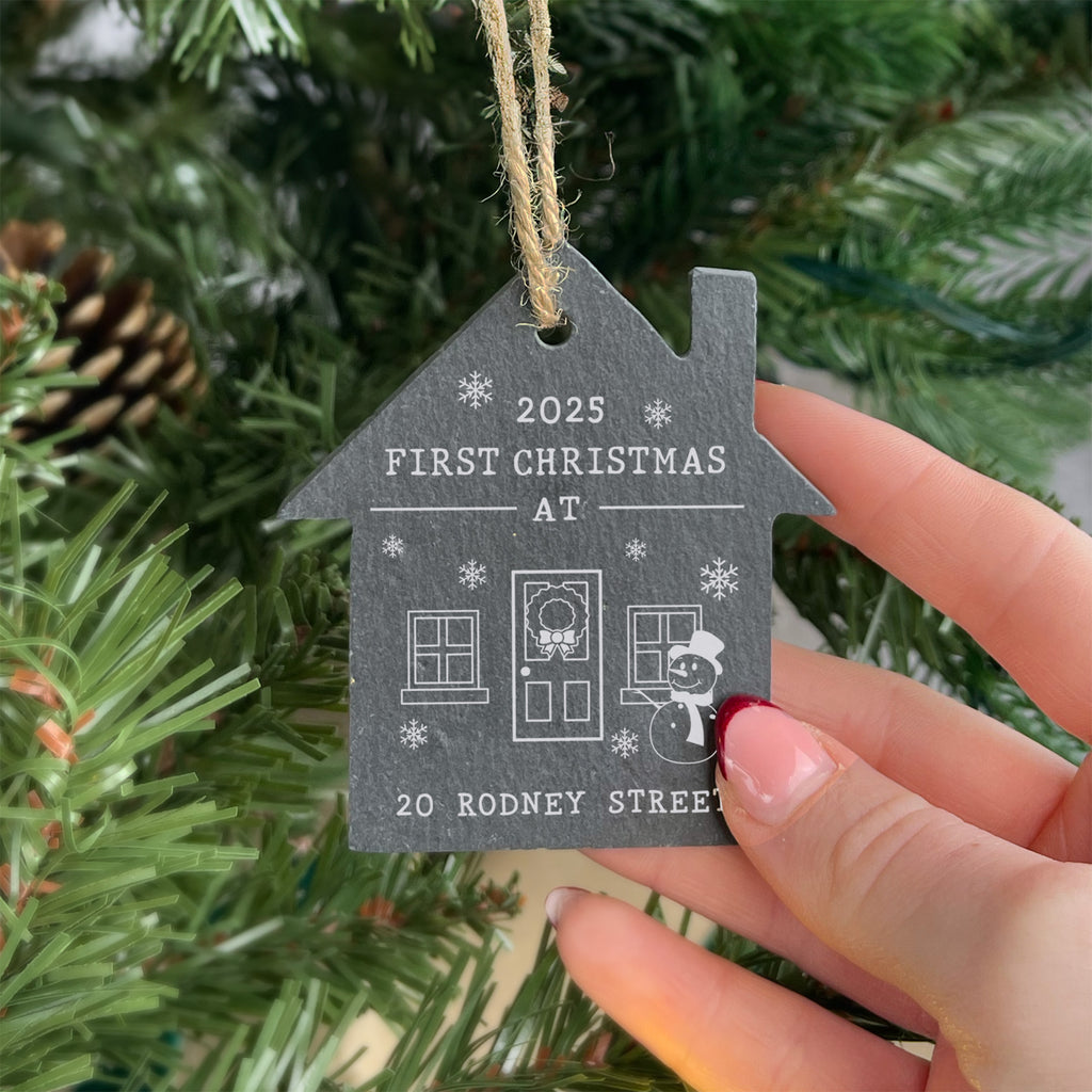 House-shaped ornament with '2025 First Christmas at 20 Rodney Street' text, held against a Christmas tree.