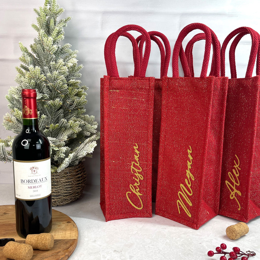 Red wine bottle bags with names and a bottle of red wine on a wooden surface.