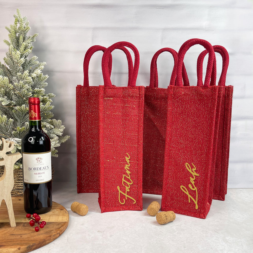 Red wine bags with personalized names next to a bottle of wine on a table.