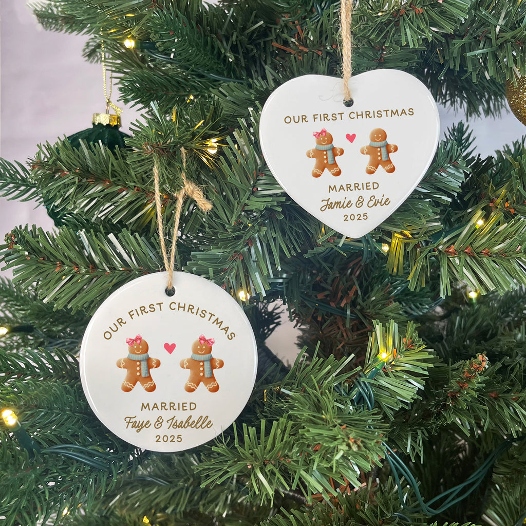Two heart-shaped ornaments with gingerbread men and text hanging on a Christmas tree.