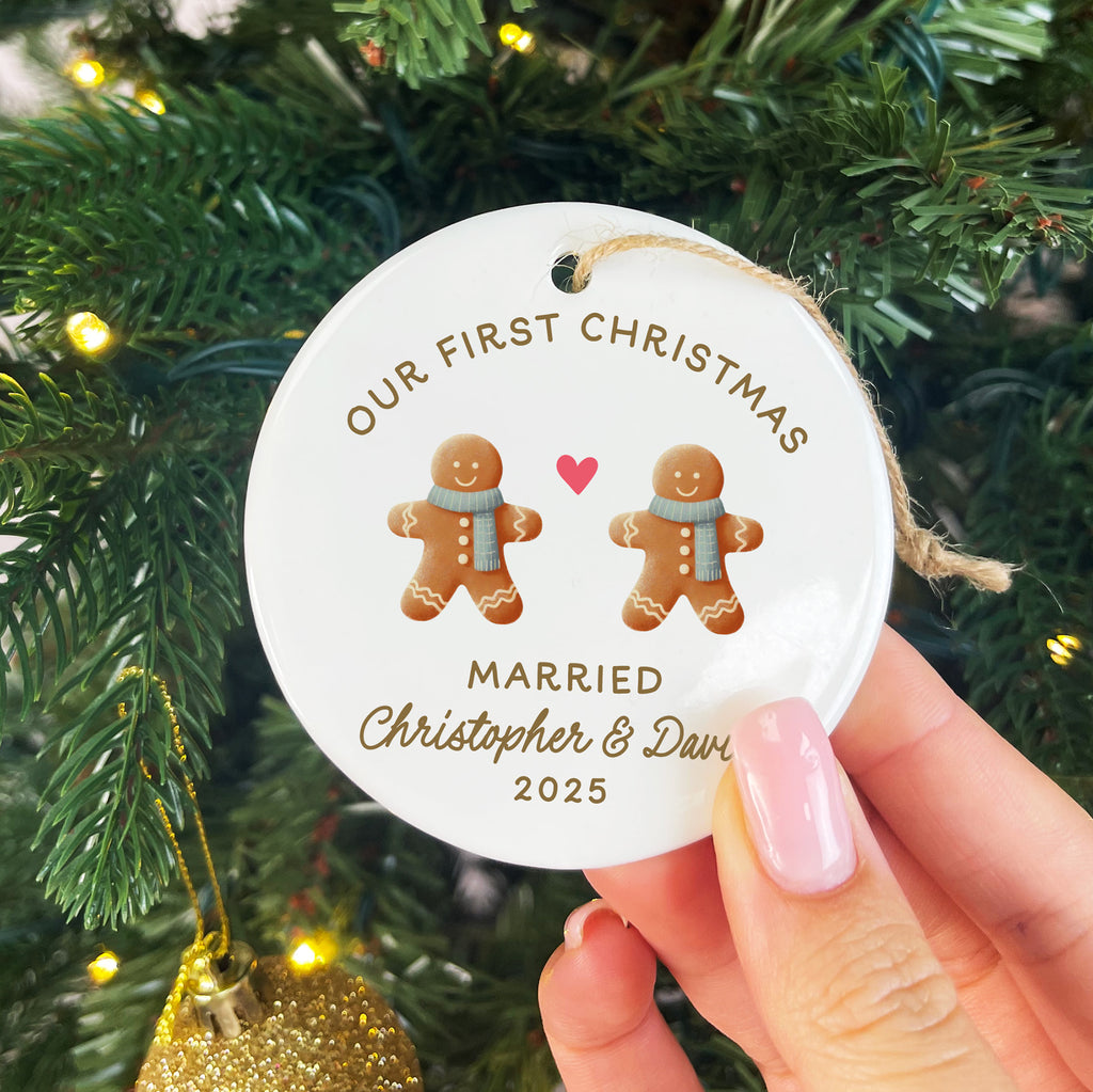 Decorative ornament with gingerbread men and text held in front of a Christmas tree.