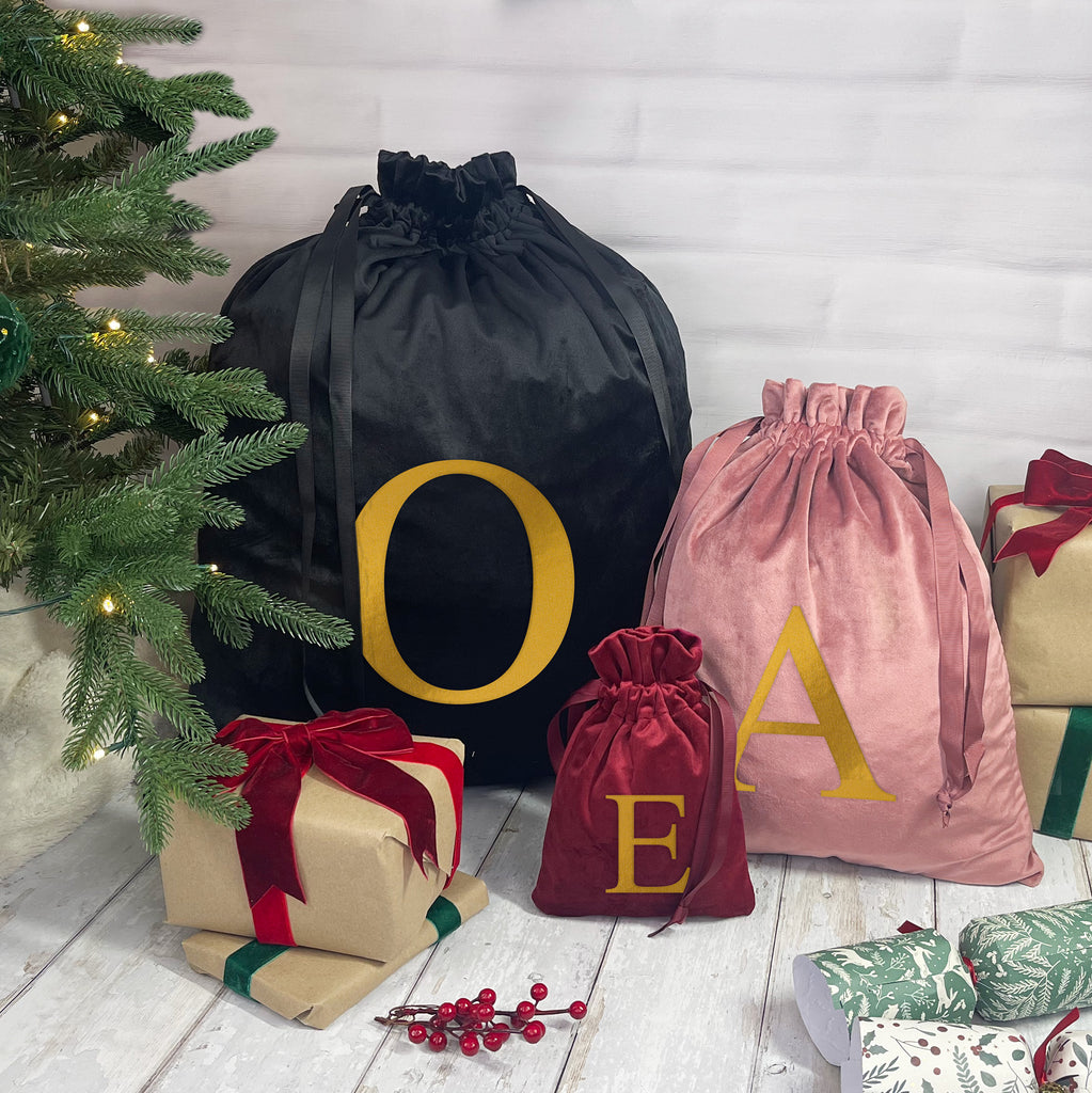 Black, pink, and red drawstring bags with gold letters next to Christmas presents and a tree.