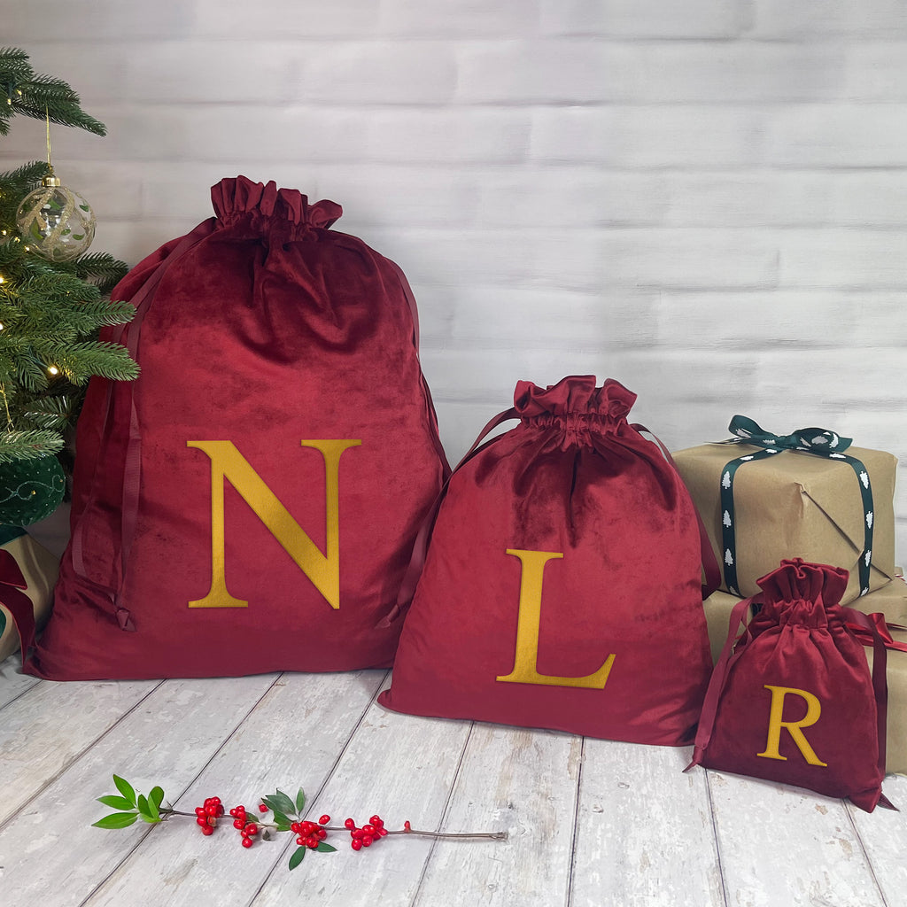 Red velvet sacks with gold letters 'N', 'L', and 'R' next to a Christmas tree and wrapped presents.