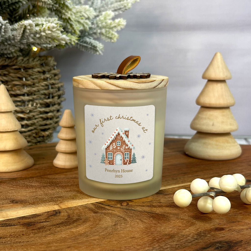 Candle with a gingerbread house design label on a wooden surface with Christmas decor.
