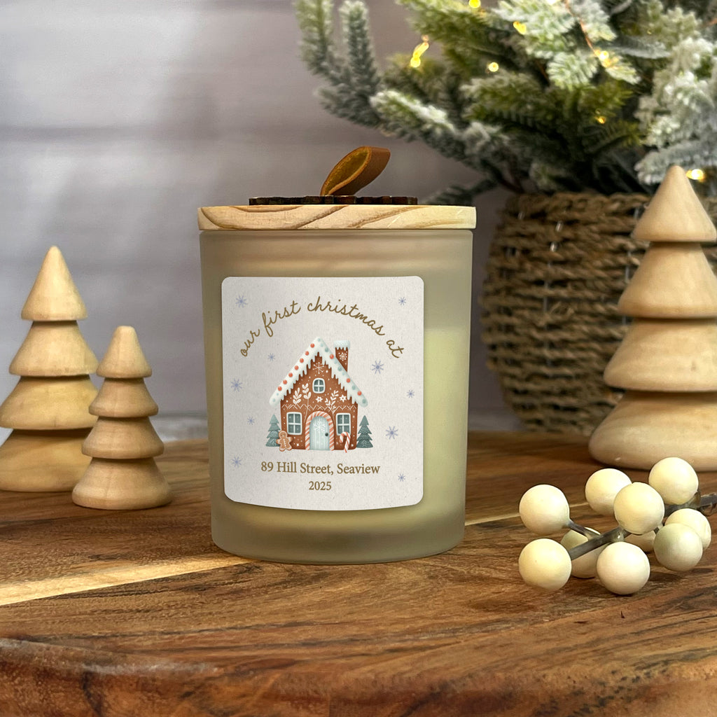 Candle with a gingerbread house label on a wooden surface with Christmas decor