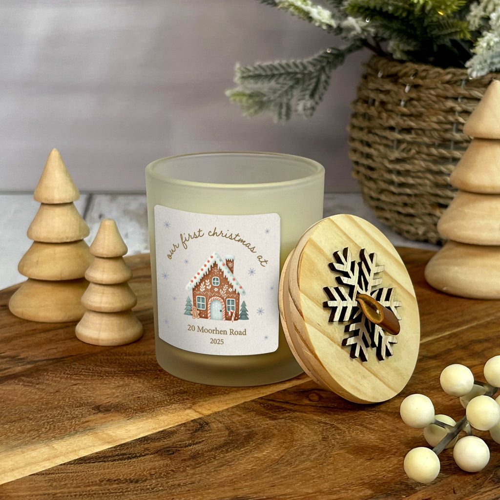 Decorative candle with a house design label on a wooden surface with Christmas decor.