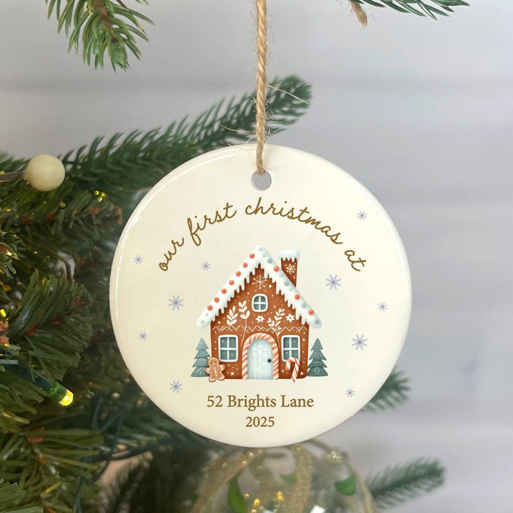 Round Christmas ornament with gingerbread house design and text, hanging on a tree.