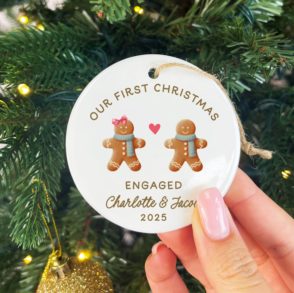 Decorative ornament with gingerbread men and text held in front of a Christmas tree.